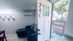 A compact living space with a kitchenette, a sofa, a red chair, and a door marked with the number 34C. - ATL: 6BR Triplex—Chic, Boho,Retro Vibes |Sleeps 16 (Atlanta)