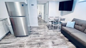 Et moderne køkken med et rustfrit stål køleskab, et spiseområde med bord og stole, og et opholdsområde med sofa og et fladskærms-tv monteret på væggen.