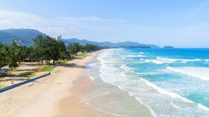 Uma praia com areal arenoso, palmeiras e oceano azul cristalino.
