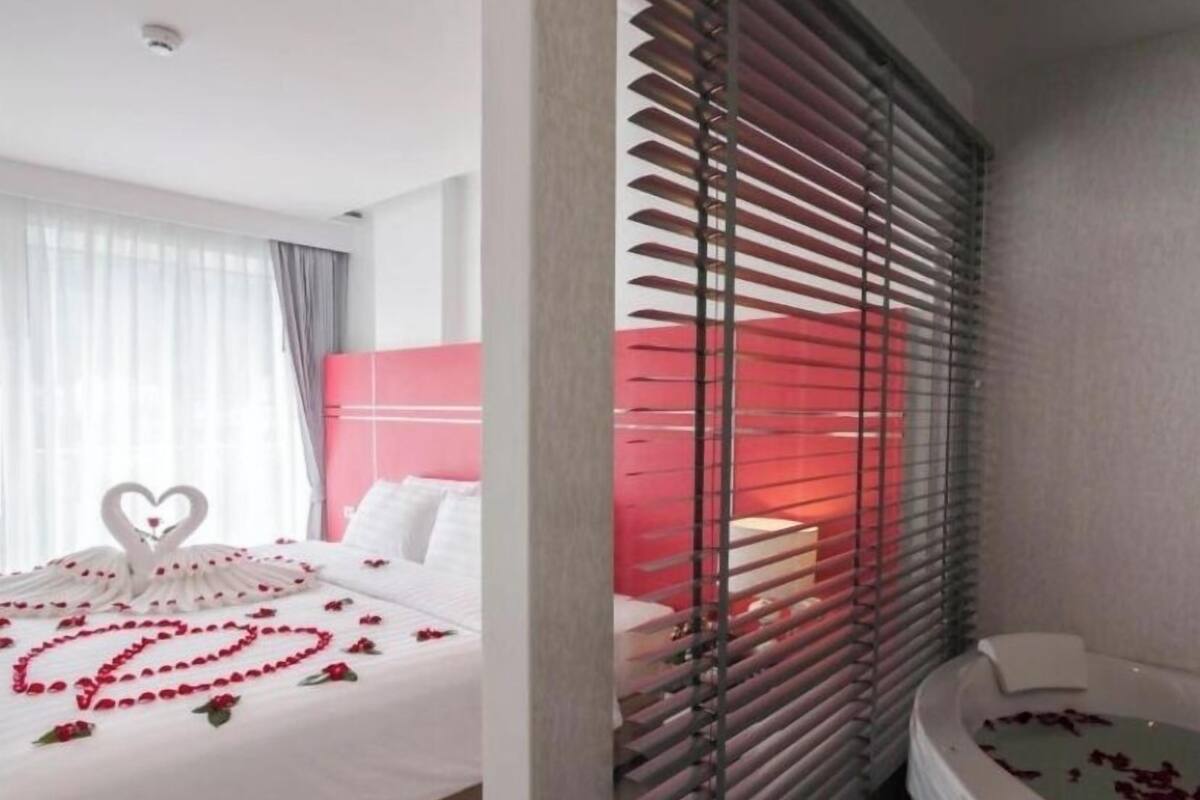 A hotel room with a bed, a red headboard, and a bathtub with rose petals.