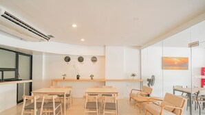 Uma sala de reunião moderna com uma mesa comprida, várias cadeiras, uma planta pequena e um relógio na parede.
