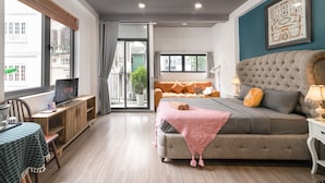 Un dormitorio moderno con una cama grande, un televisor sobre una consola de madera, una mesa de comedor y vistas a través de un ventanal.