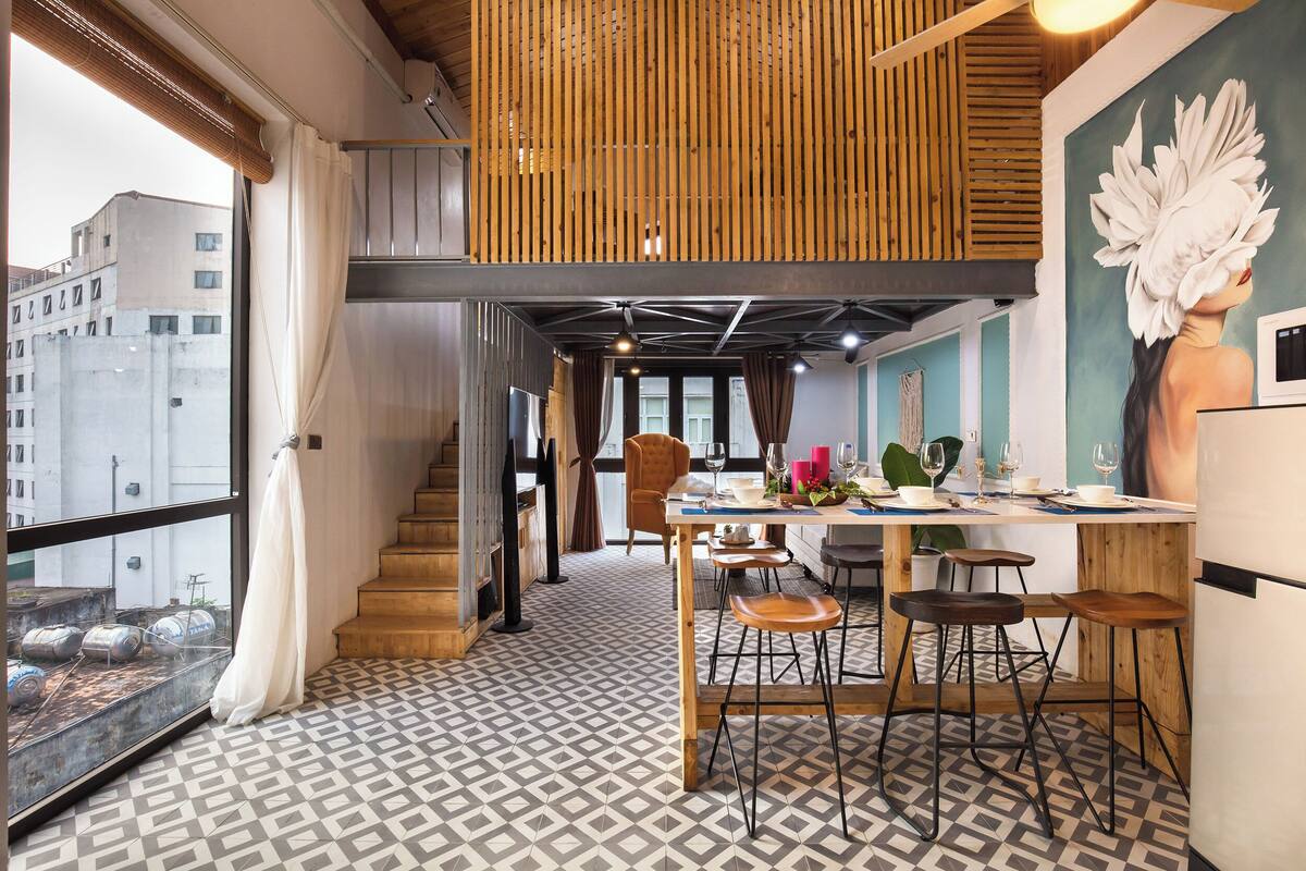 A modern kitchen with a dining area, wooden accents, and a large window overlooking a cityscape.