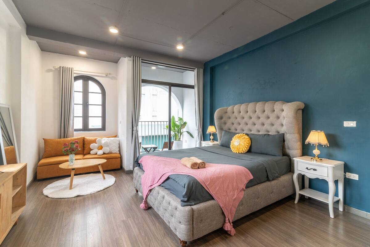 A bedroom with a bed, a sofa, a nightstand, a lamp, and a window with curtains.