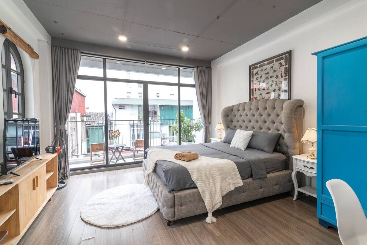 A modern bedroom with a large bed, a desk, and a view of the outside.
