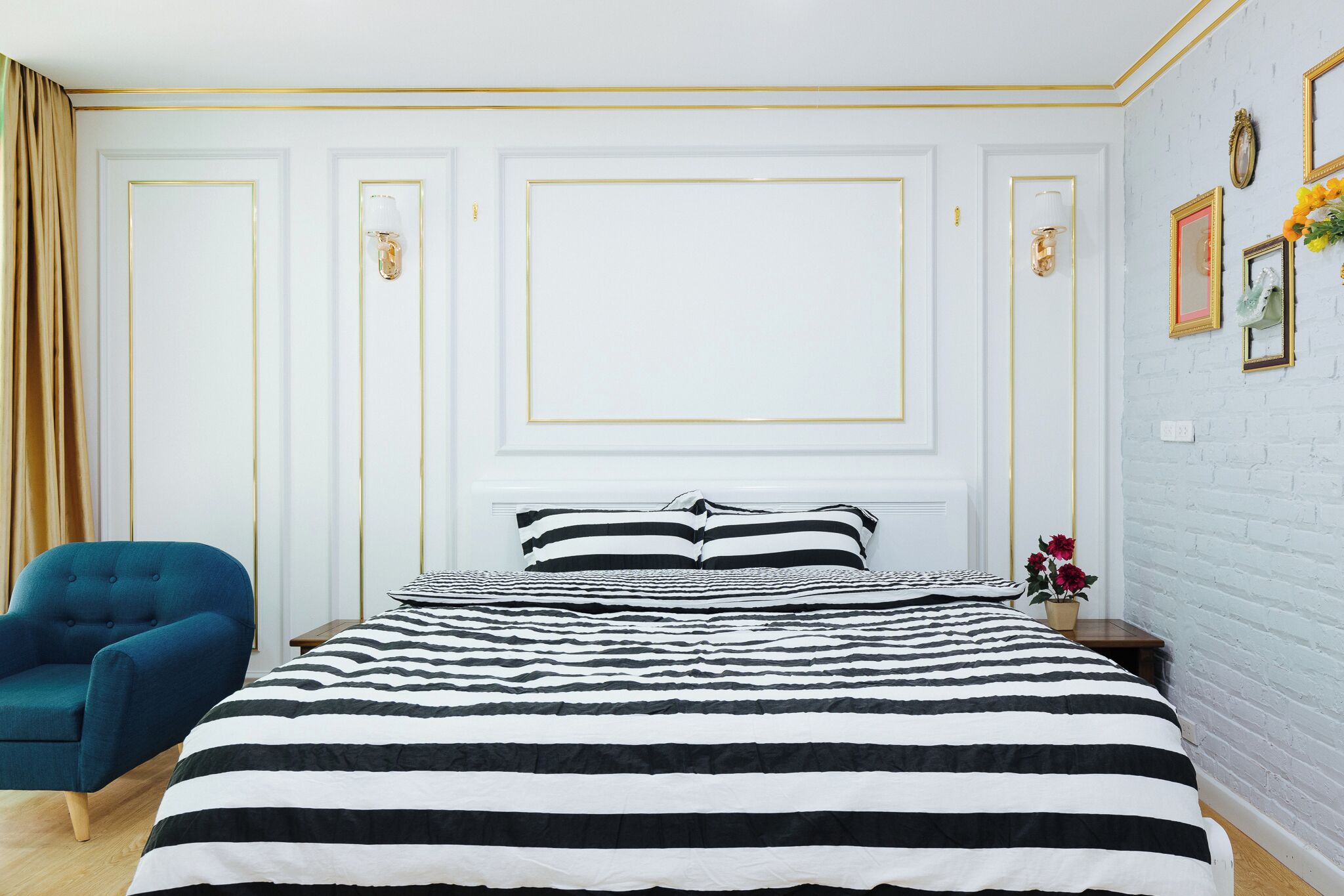 A bedroom with a large bed, a blue armchair, and a white brick wall with framed pictures.