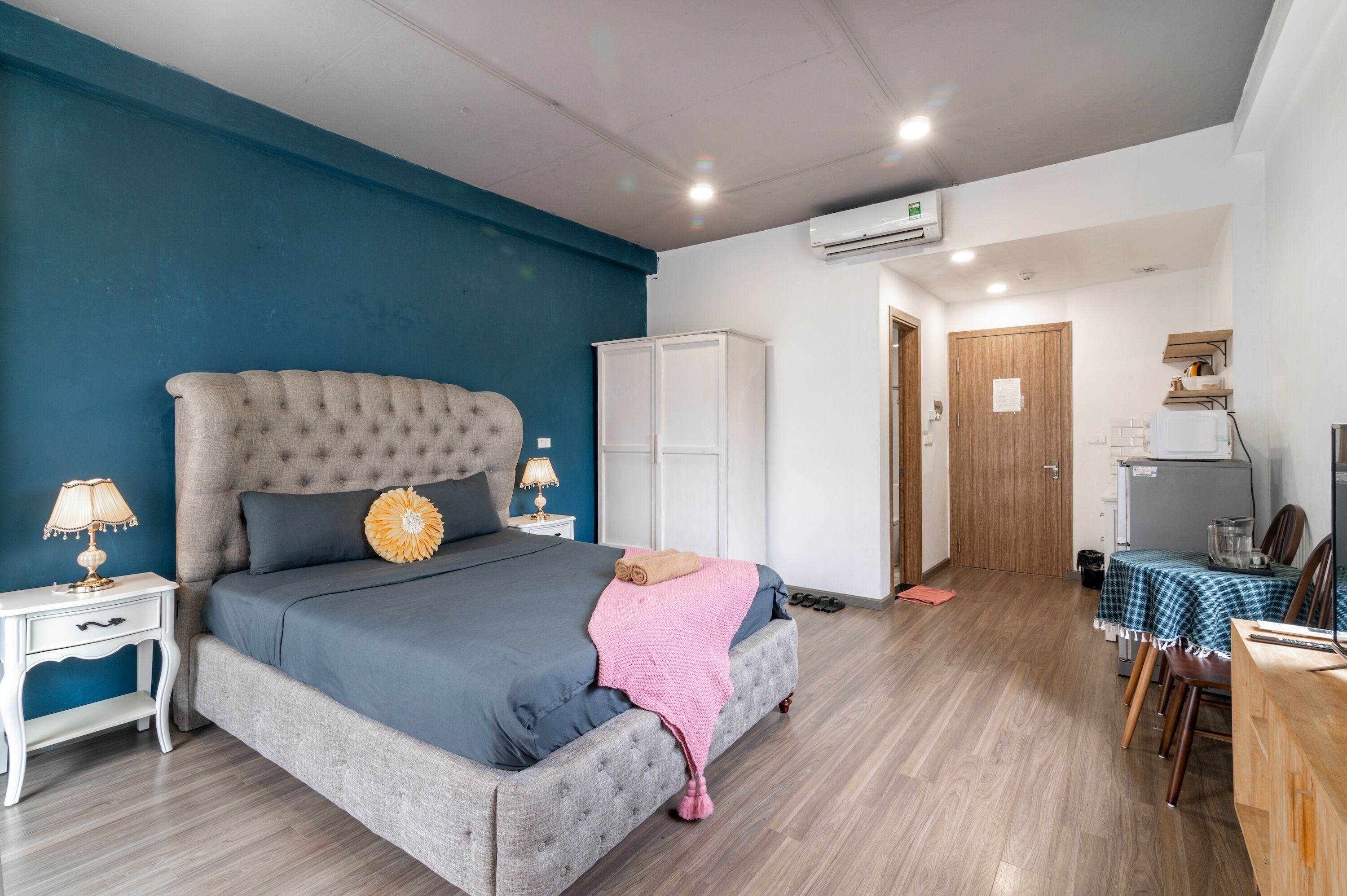 A bedroom with a large bed, a nightstand, a wardrobe, and a kitchenette area.
