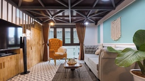 Un salón acogedor con sofá, sillón y mesa de centro. Hay un televisor sobre un mueble de madera y una planta grande en la esquina.