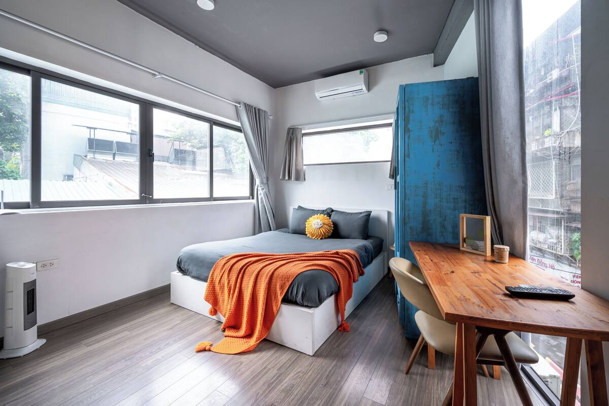 A modern bedroom with a bed, a wooden desk, and a window with curtains.