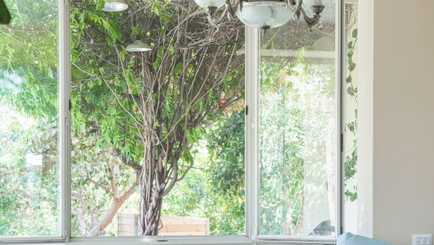 A room with a large window, a wooden table with a lace tablecloth, a patterned rug, and a blue pillow on a sofa. - Artistic Vac Villa w pool by Sea N' Rent (Rishon LeTsiyon)
