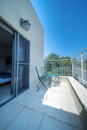 A balcony with a table and chairs, a sliding glass door leading to a bedroom, and a street view with trees in the background. - Artistic Vac Villa w pool by Sea N' Rent (Rishon LeTsiyon)
