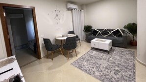 Ein modernes Wohnzimmer mit Essbereich, einem grauen Sofa, einem weißen Couchtisch und einem grauen Teppich.