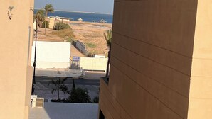 Blick von einem Balkon auf einen Sandstrand bei blauem Himmel.