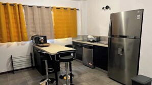 Eine kleine Küche mit Kühlschrank, Kaffeemaschine, Spüle und zwei Barhocker.