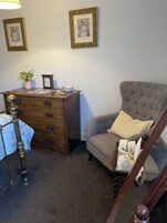 A room with a wooden dresser, a grey armchair, a small table with a bowl, a potted plant, and two framed pictures on the wall.
