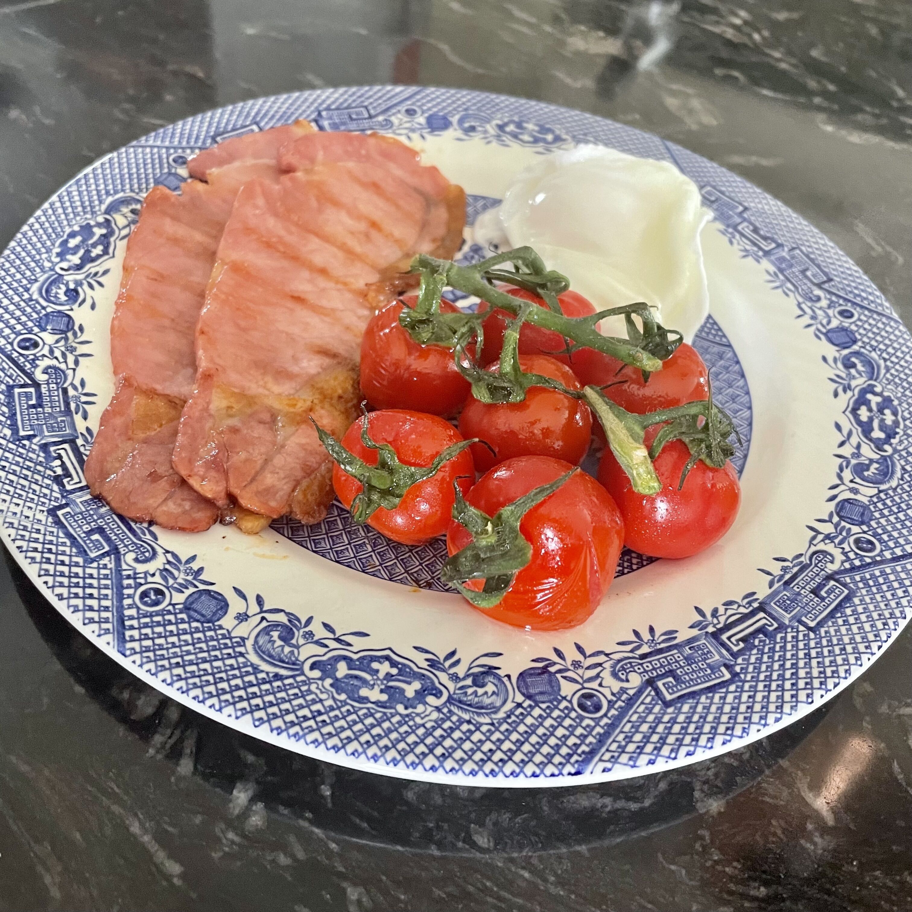 Un plato con carne en rodajas, tomates cherry y una cucharada de crema sobre un plato estampado.