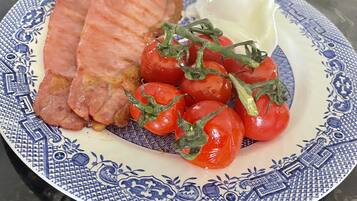 Un plato con carne en rodajas, tomates cherry y una cucharada de crema sobre un plato estampado.