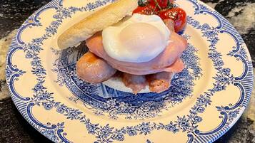 Un piatto con uovo in camicia, salsiccia e pomodoro alla griglia su una pirofila decorata.