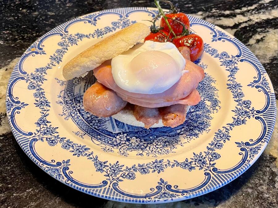 Un piatto con uovo in camicia, salsiccia e pomodoro alla griglia su una pirofila decorata.