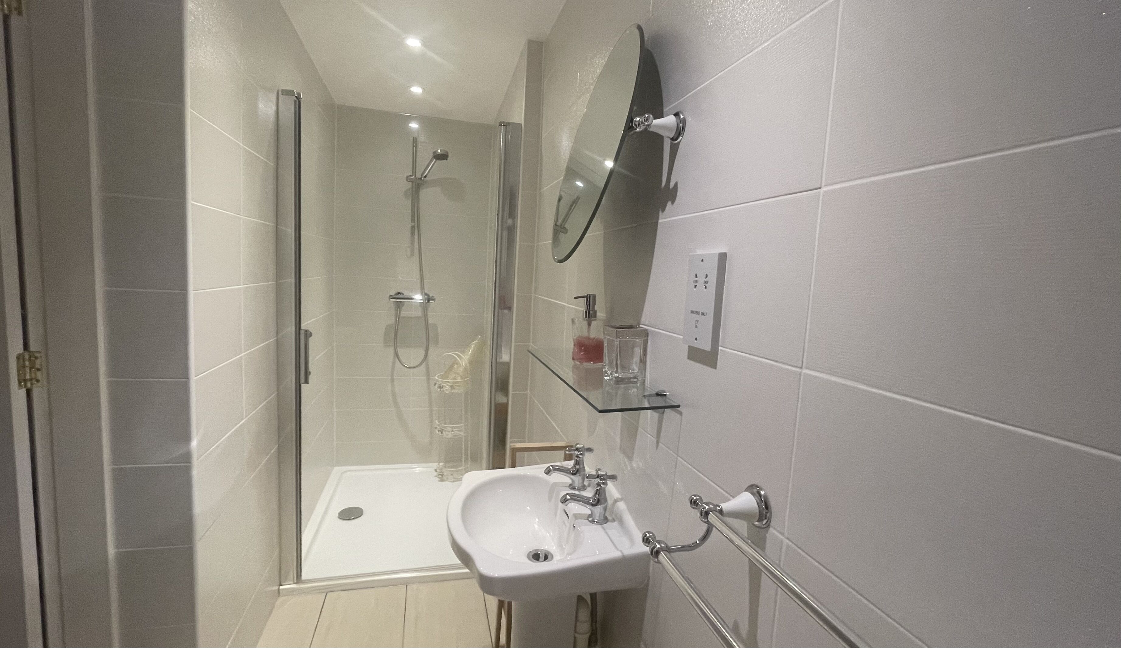 Une salle de bain moderne avec une douche à parois de verre, un lavabo sur colonne et un miroir fixé au mur.