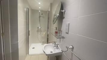 Un baño moderno con cabina de ducha de vidrio, lavamanos sobre pedestal y espejo fijado a la pared.