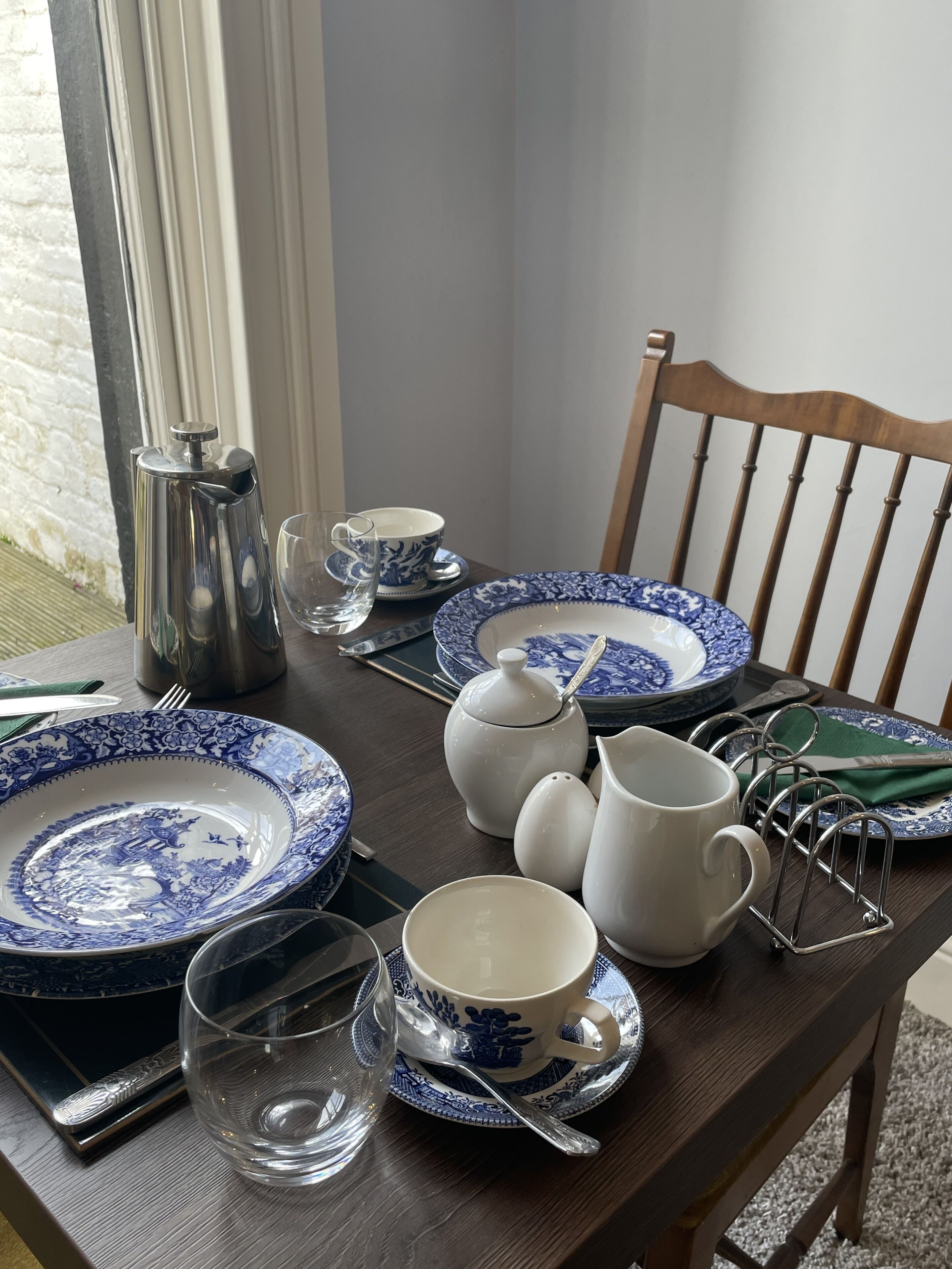 Una mesa de comedor con platos de diseño azul y blanco, una jarrón, una taza y un vaso.