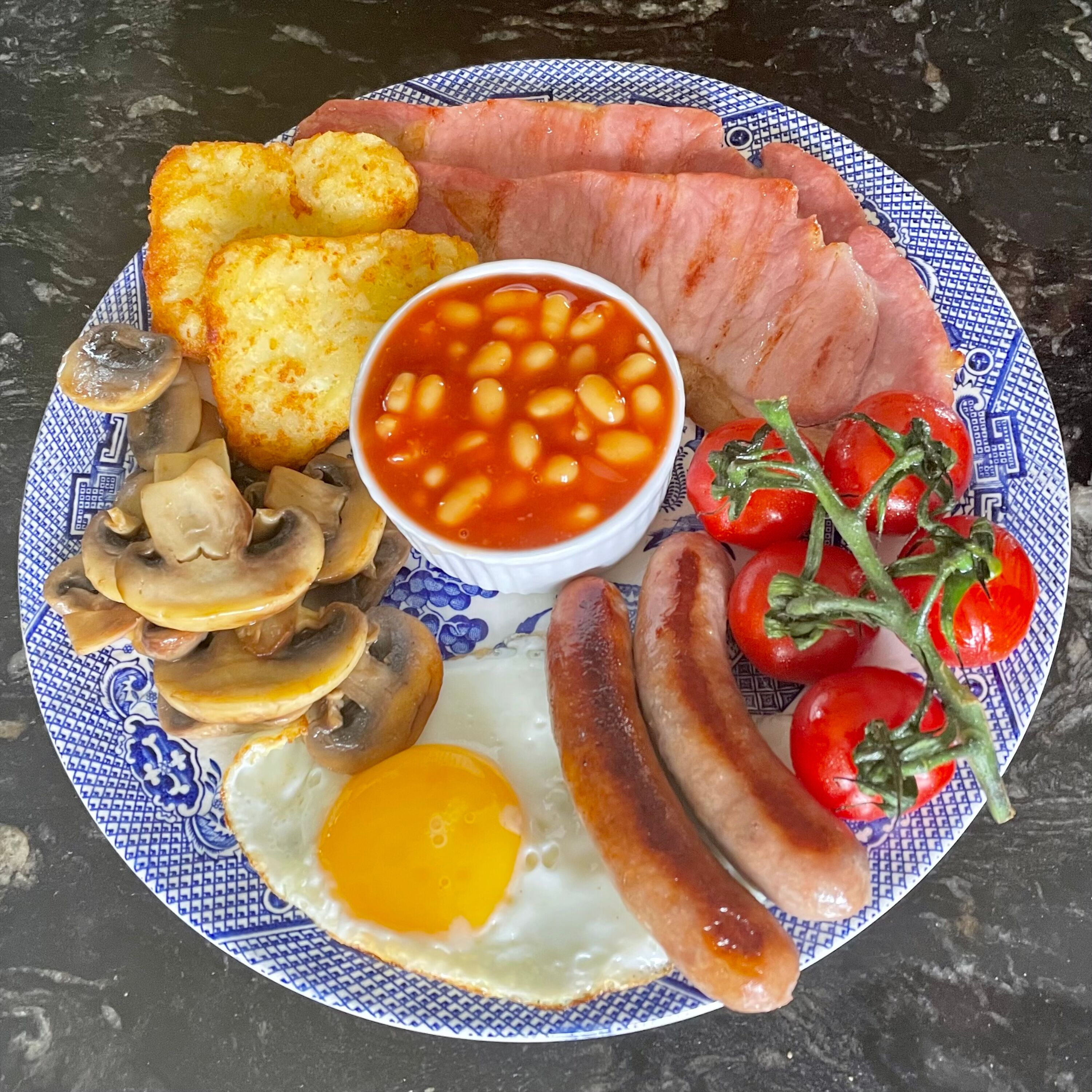 Un plato de comida para el desayuno con salchichas, huevos, champiñones, frijoles, tomates y tostadas.