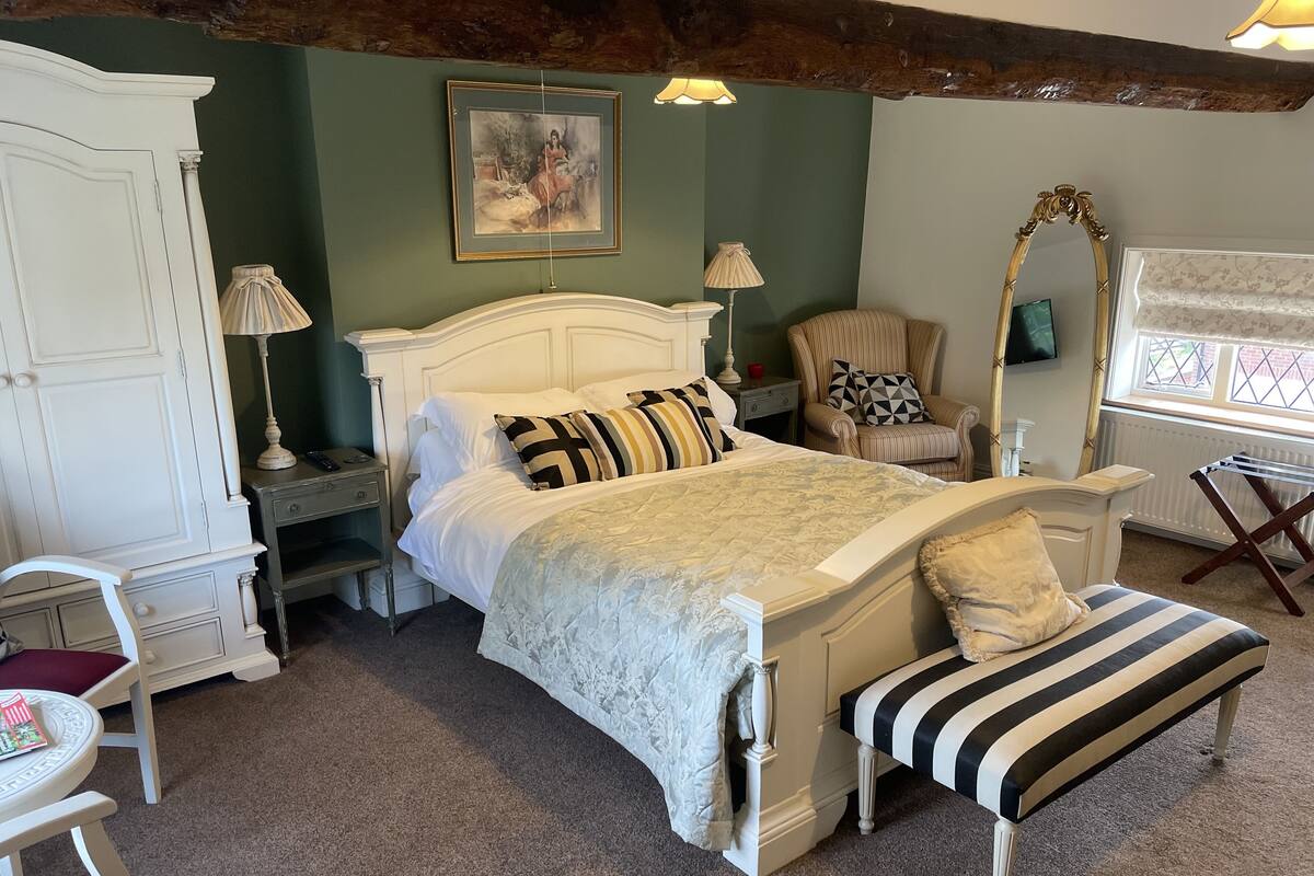 A bedroom with a large bed, a chair, a wardrobe, a mirror, and a window.