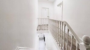 A white interior hallway with a staircase leading to a door at the end. - Modern Room in Centrally Located- Room 4 (London)