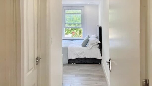 A narrow hallway leading to a bedroom with a bed, a window, and a door. - Modern Room in Centrally Located- Room 4 (London)