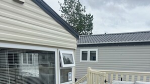 A covered outdoor deck with a wicker sofa, a small table, and a railing. - Lovely 2-bed Cabin in Birchington (Birchington)