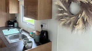 A compact kitchenette with wooden cabinets, a sink, a coffee maker, and a decorative wreath. - Lovely 2-bed Cabin in Birchington (Birchington)