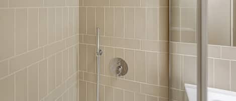 A bathroom with beige tiled walls, a glass shower enclosure, and a white sink.