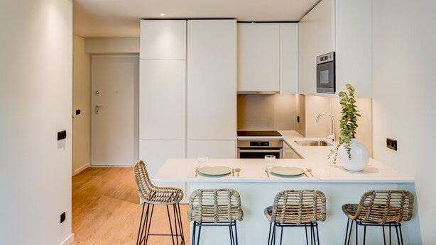 A modern kitchen with white cabinetry, a central island with bar stools, and a built-in oven.