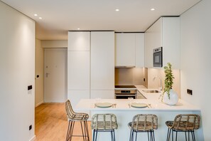 A modern kitchen with white cabinetry, a central island with bar stools, and a built-in oven. - Blissful Suites Porto by gaiarooms (Porto)