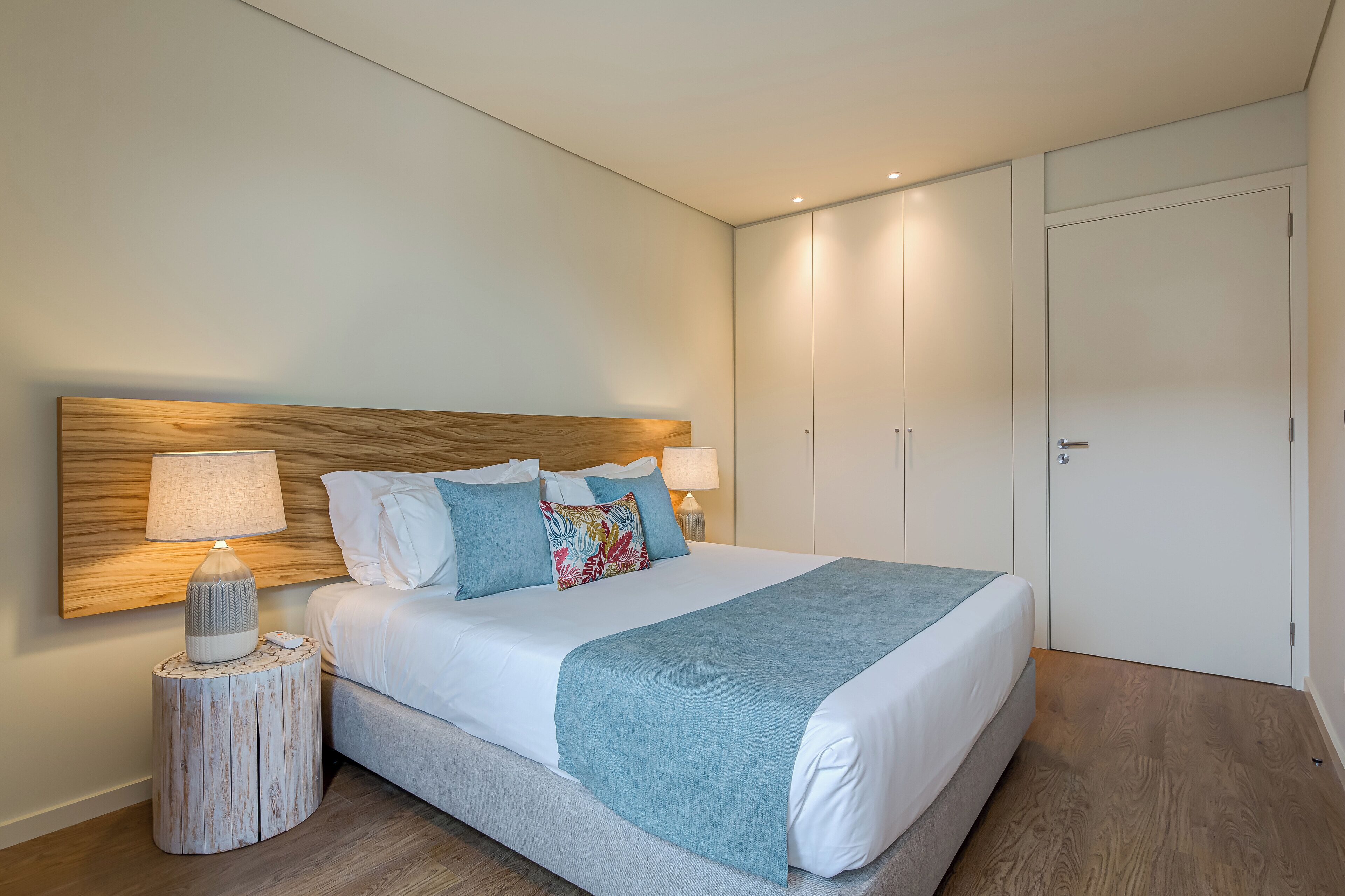 A neatly made bed with a wooden headboard, a bedside table with a lamp, and a large wardrobe.
