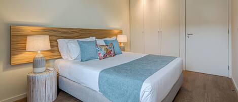 A neatly made bed with a wooden headboard, a bedside table with a lamp, and a large wardrobe.