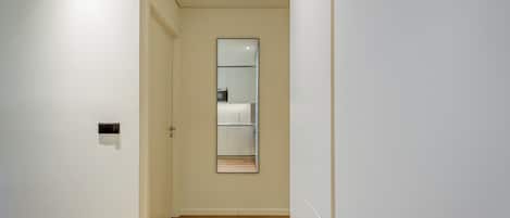 A narrow hallway with a wooden floor, a door on the left, and a large mirror on the right.