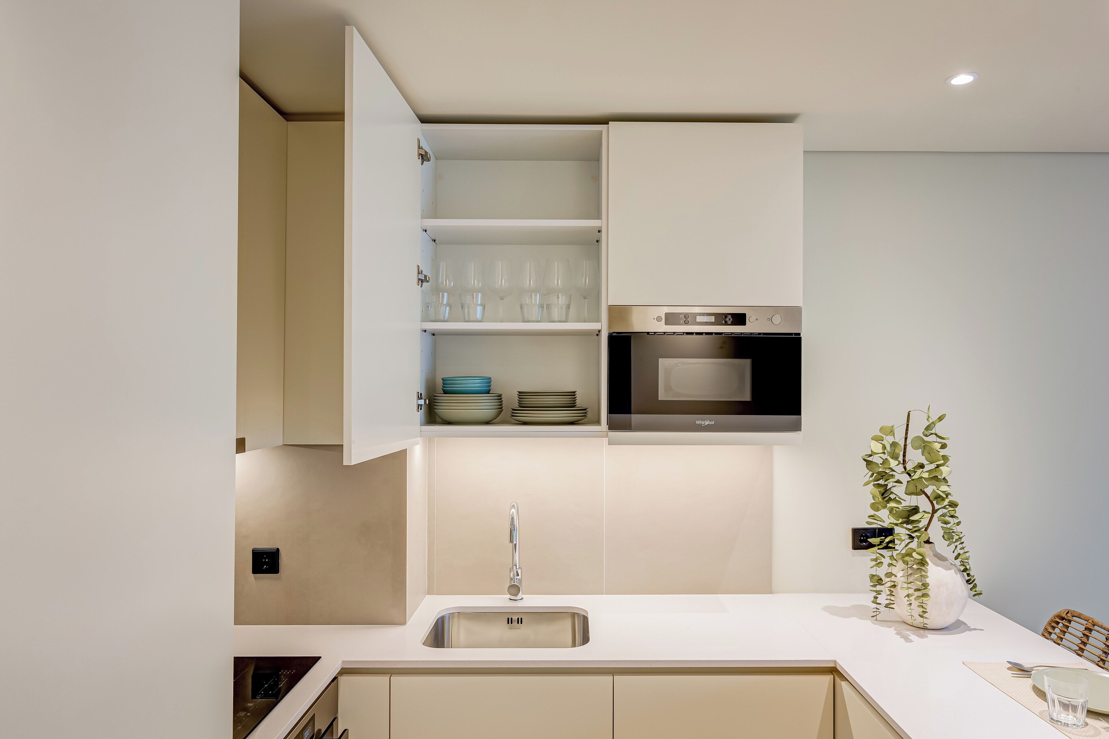 A modern kitchen with a built-in oven, a stainless steel sink, and a white countertop.