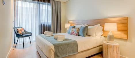 Une chambre d’hôtel moderne avec un grand lit, une chaise, une table de chevet et une fenêtre avec des rideaux.