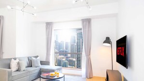 Ein modernes Wohnzimmer mit einem grauen Sofa, einem Couchtisch mit einer Zeitschrift und Orangensaft, einem großen Fenster mit Vorhängen und einem an der Wand befestigten Fernseher, der das Netflix-Logo zeigt.