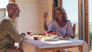 Uma cabana de madeira com uma mesa de jantar posta para dois, incluindo uma refeição, vinho e vista para o exterior.