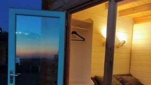 Uma cabana de madeira com porta de correr de vidro que dá para um quarto com cama e cômoda.