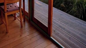 Um deck de madeira com mesa e cadeiras, com vista para uma paisagem e um pôr do sol.