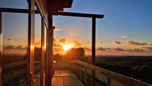Um deck de madeira com vista para o pôr do sol sobre a paisagem.