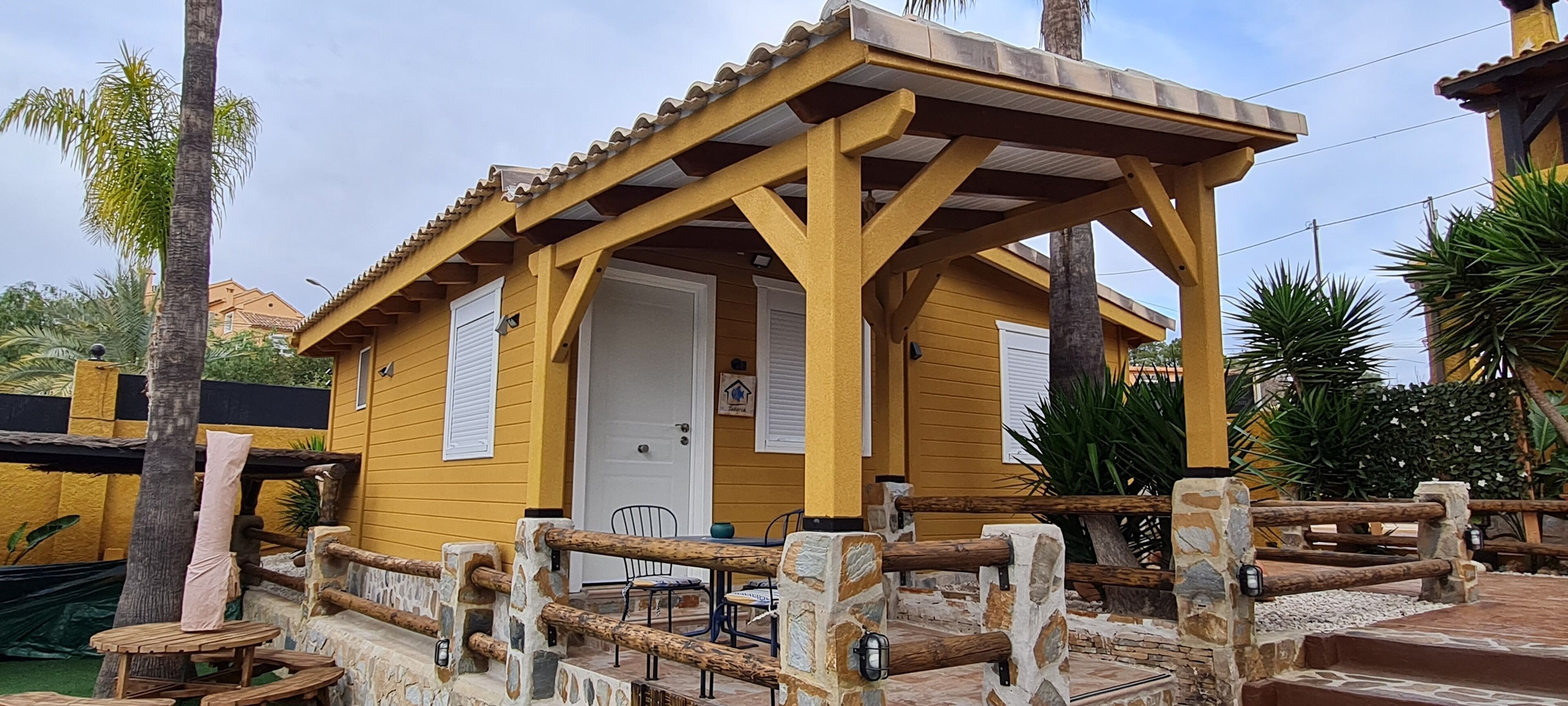 Een geel gebouw met een overdekte patio, stenen muren en een houten hek.