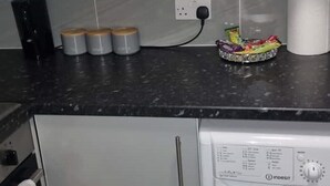 Cucina compatta con lavatrice, un piano di lavoro con barattoli e una presa di corrente.