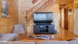 Un interior de fusta amb una escala, un televisor de pantalla plana, un sofà i un llibre a terra.