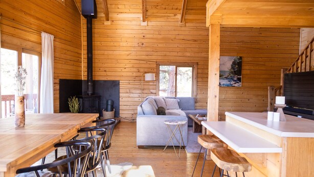 Interior d'una cabana de fusta amb zona de menjador, sofà, xemeneia i taulell de cuina.