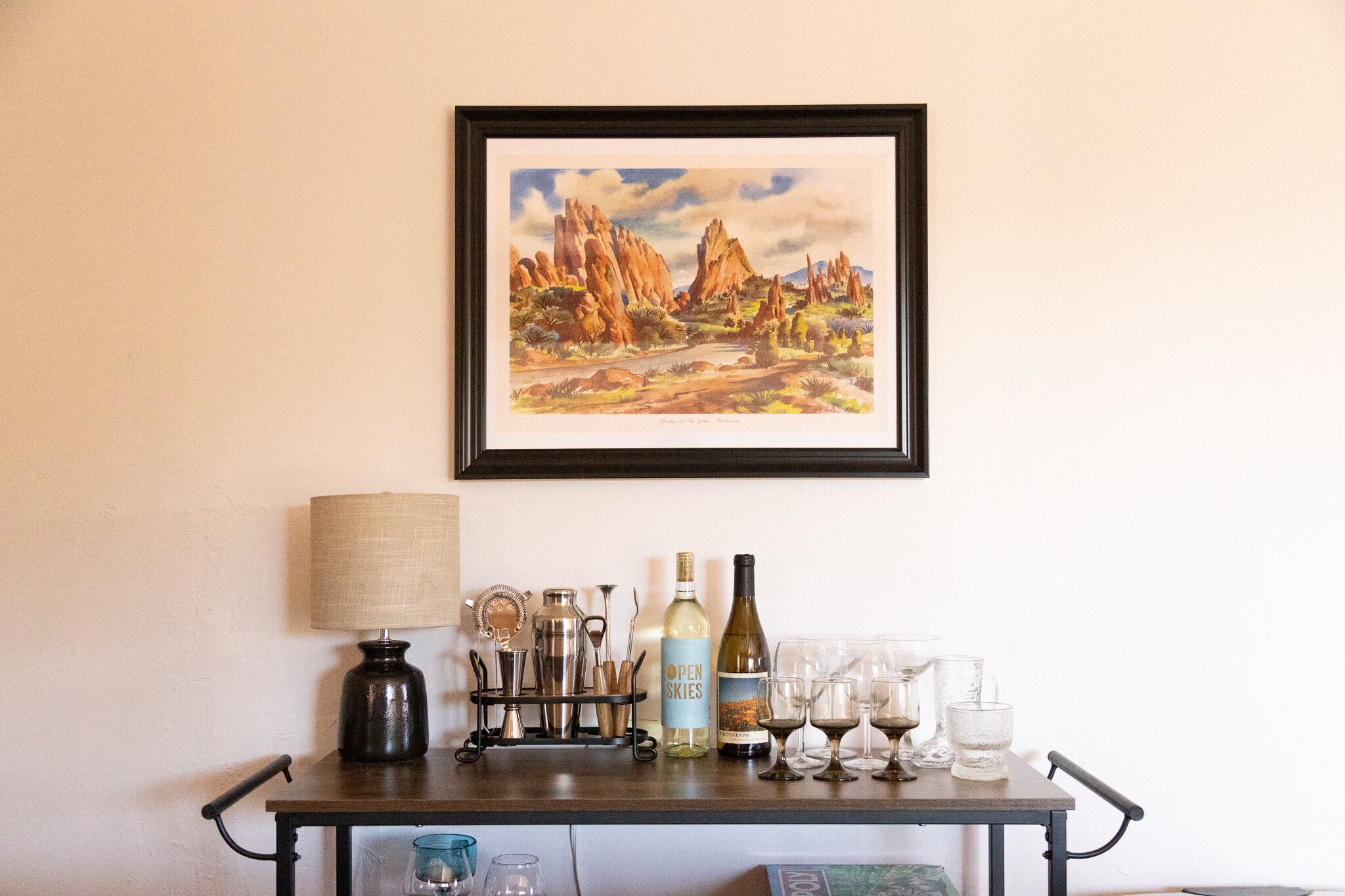 A bar area with a wine bottle, glasses, and a framed painting on the wall.